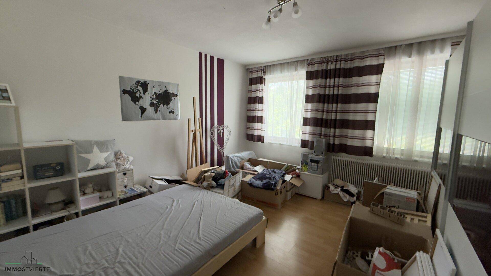 Schlafzimmer mit Holzboden, großem Fenster und einfacher Einrichtung, bereit zur persönlichen Gestaltung.