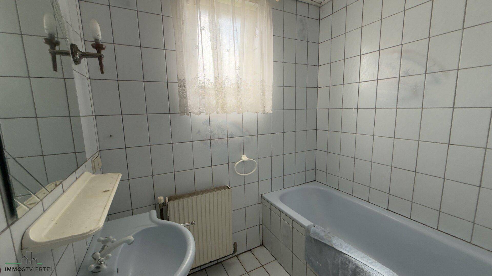 Badezimmer mit hellblauen Fliesen, Badewanne und Waschbecken, in einem älteren Zustand.