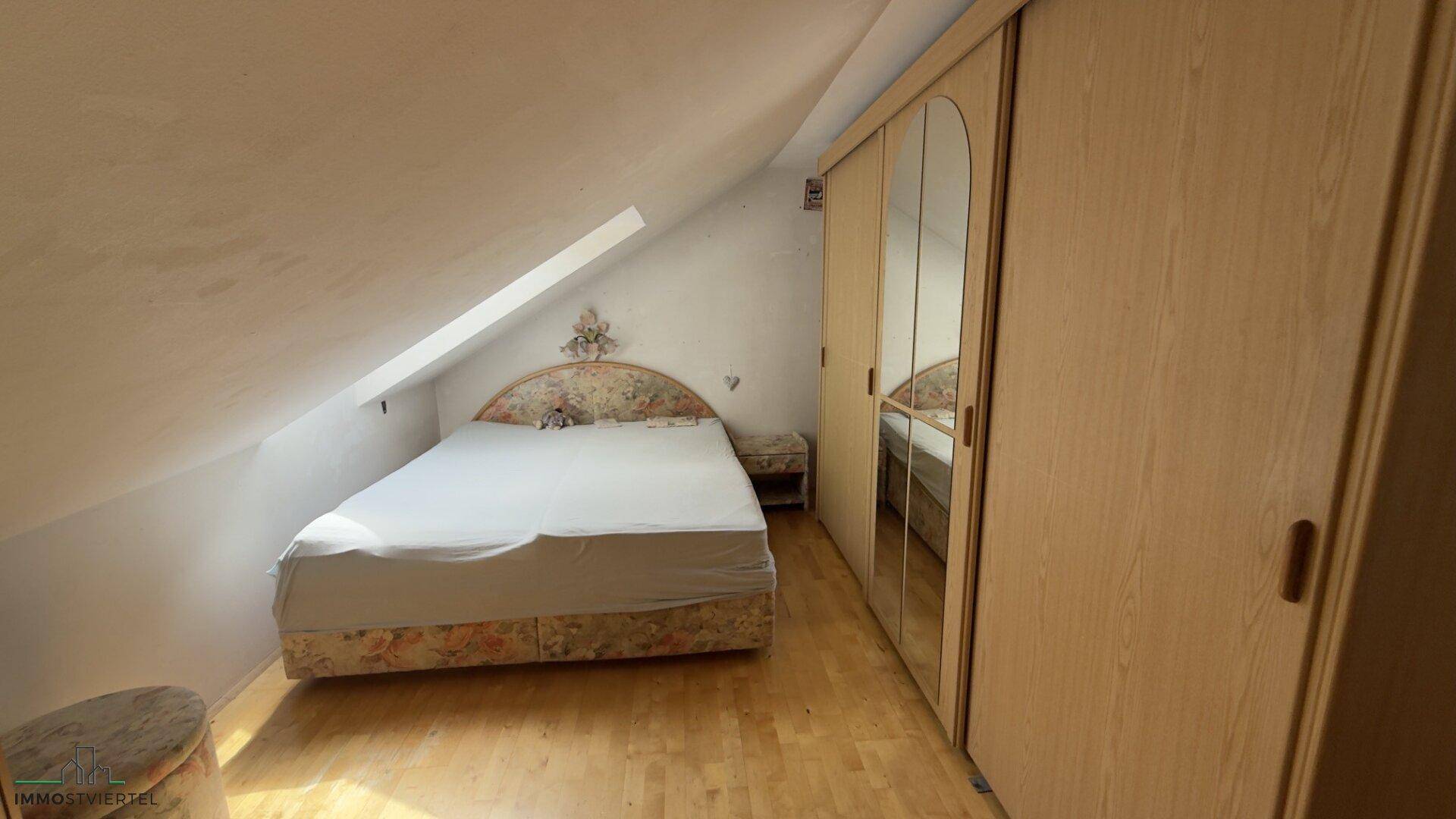 Schlafzimmer im Dachgeschoss mit Dachschräge, Holzboden und Einbauschränken, bietet gemütlichen Wohnraum.