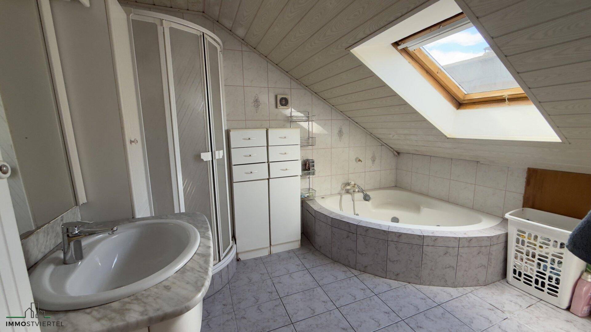 Badezimmer im Dachgeschoss mit Eckbadewanne, Dusche und Dachfenster, bietet viel natürliches Licht.
