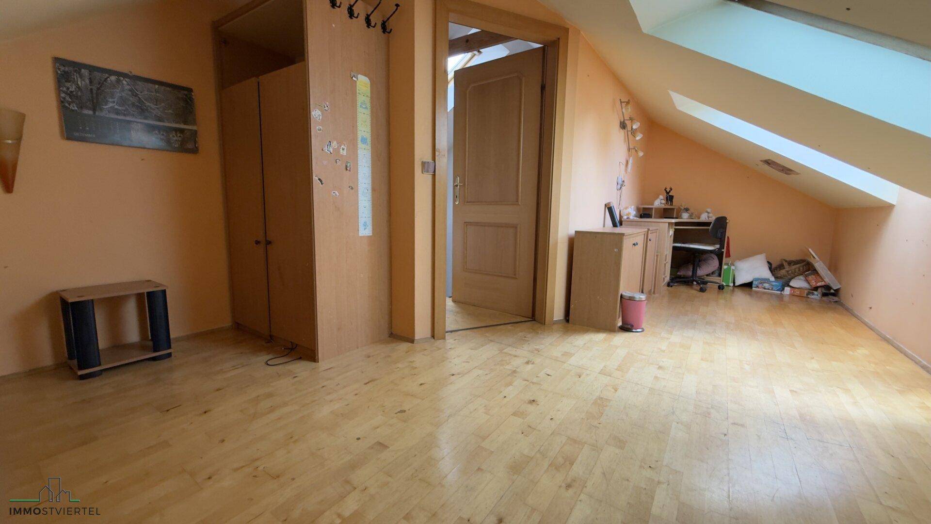 Geräumiges Dachzimmer mit Holzfußboden, Dachschrägen und einem Arbeitsbereich.