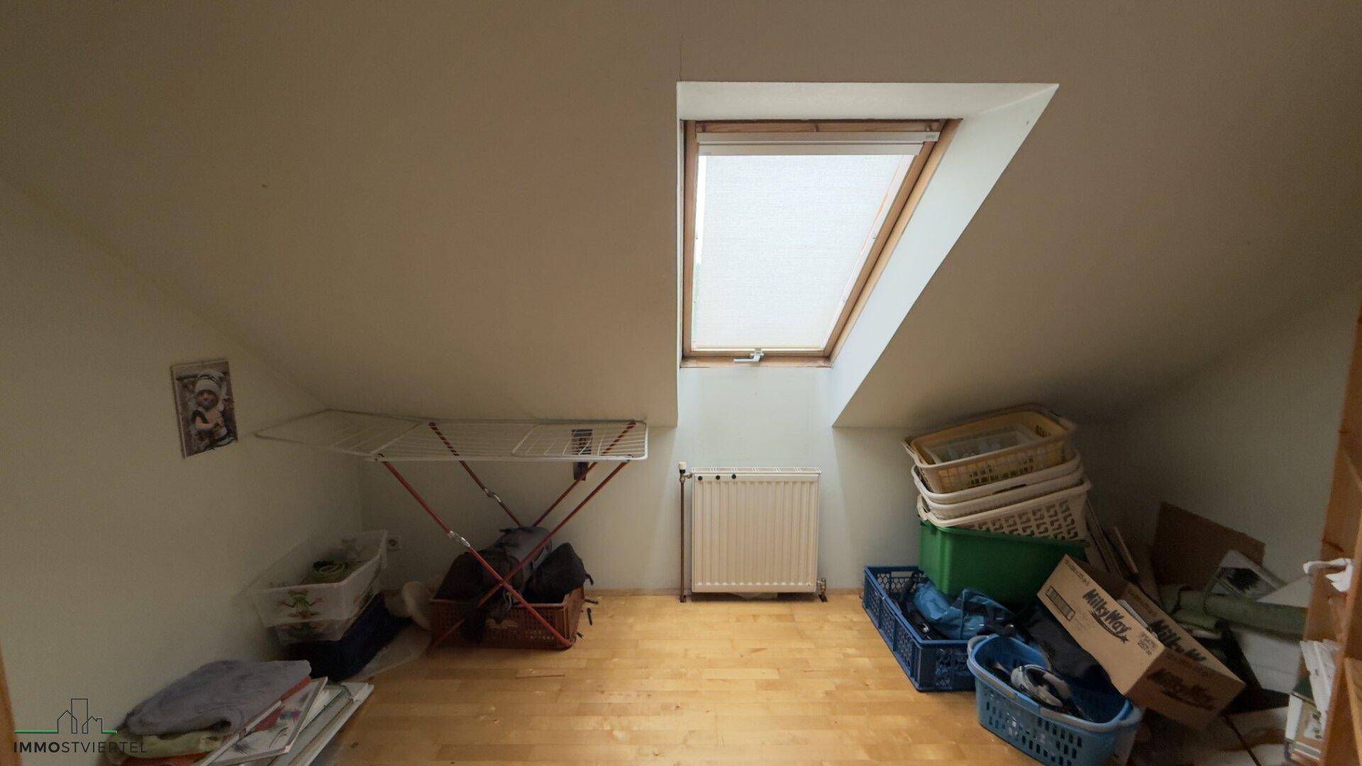 Dachbodenraum mit Dachfenster, Heizkörper und Stauraum für Haushaltsgegenstände.