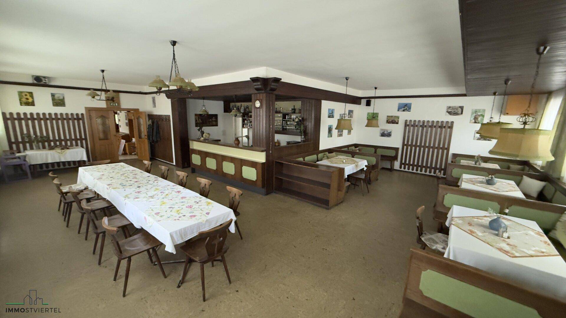 Geräumiger Speisesaal mit Holzbänken, Tischen und einer Bar, ideal für größere Veranstaltungen.