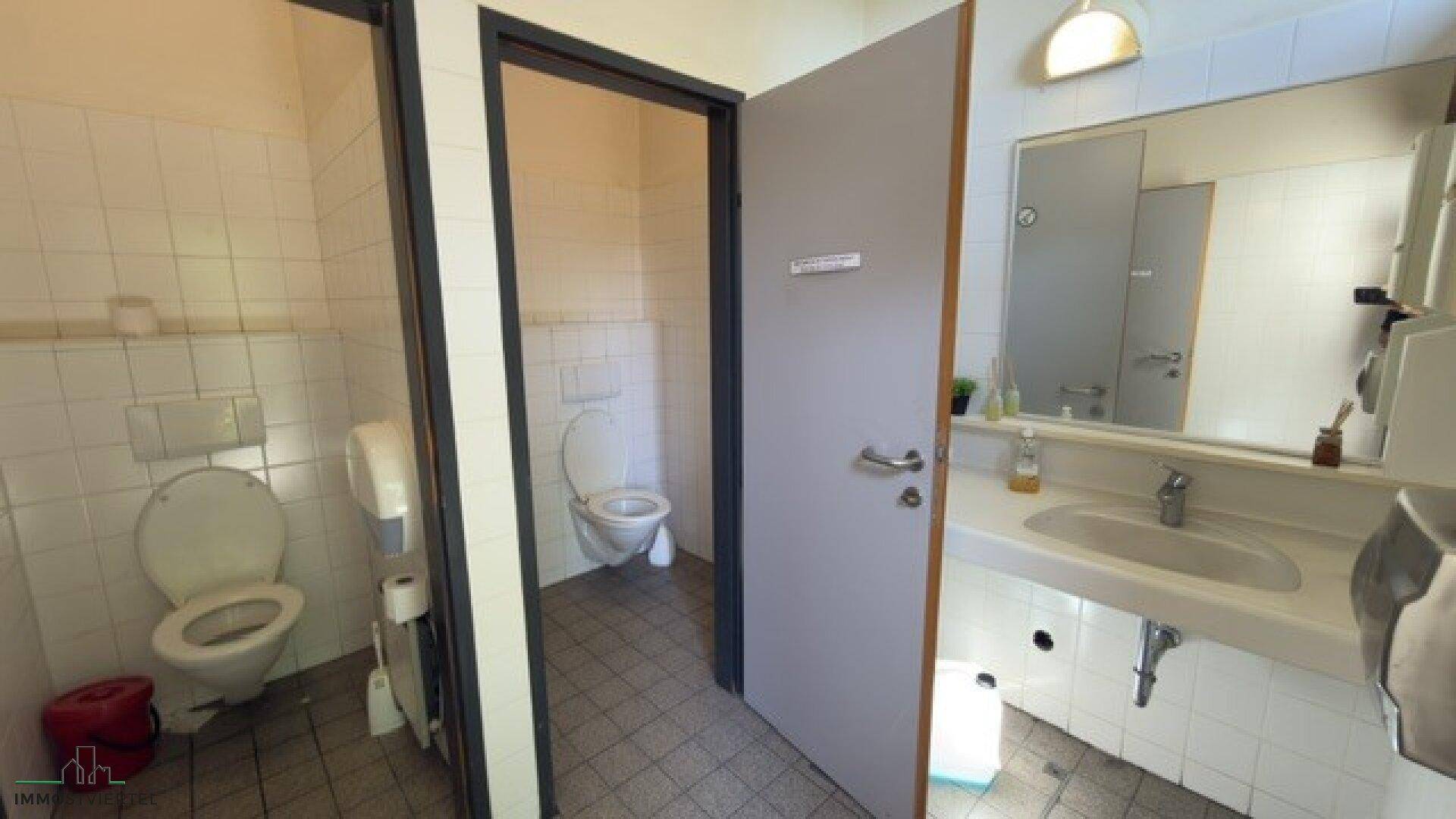 Sauberer Toilettenbereich mit mehreren Kabinen, Waschbecken und Fliesen an Wänden und Boden.