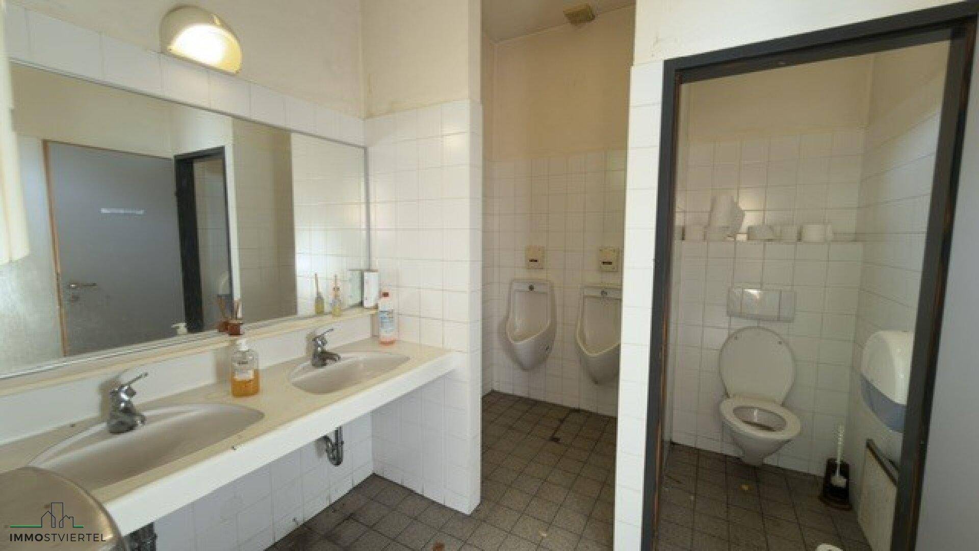 Herren-Toilettenbereich mit Waschbecken, Spiegel und Urinalen, alles in gutem, funktionalem Zustand.