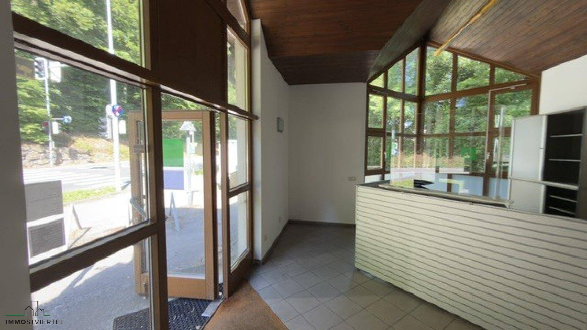 Heller Empfangsbereich mit großen Glasfenstern, die viel Tageslicht hereinlassen, und einer Theke.