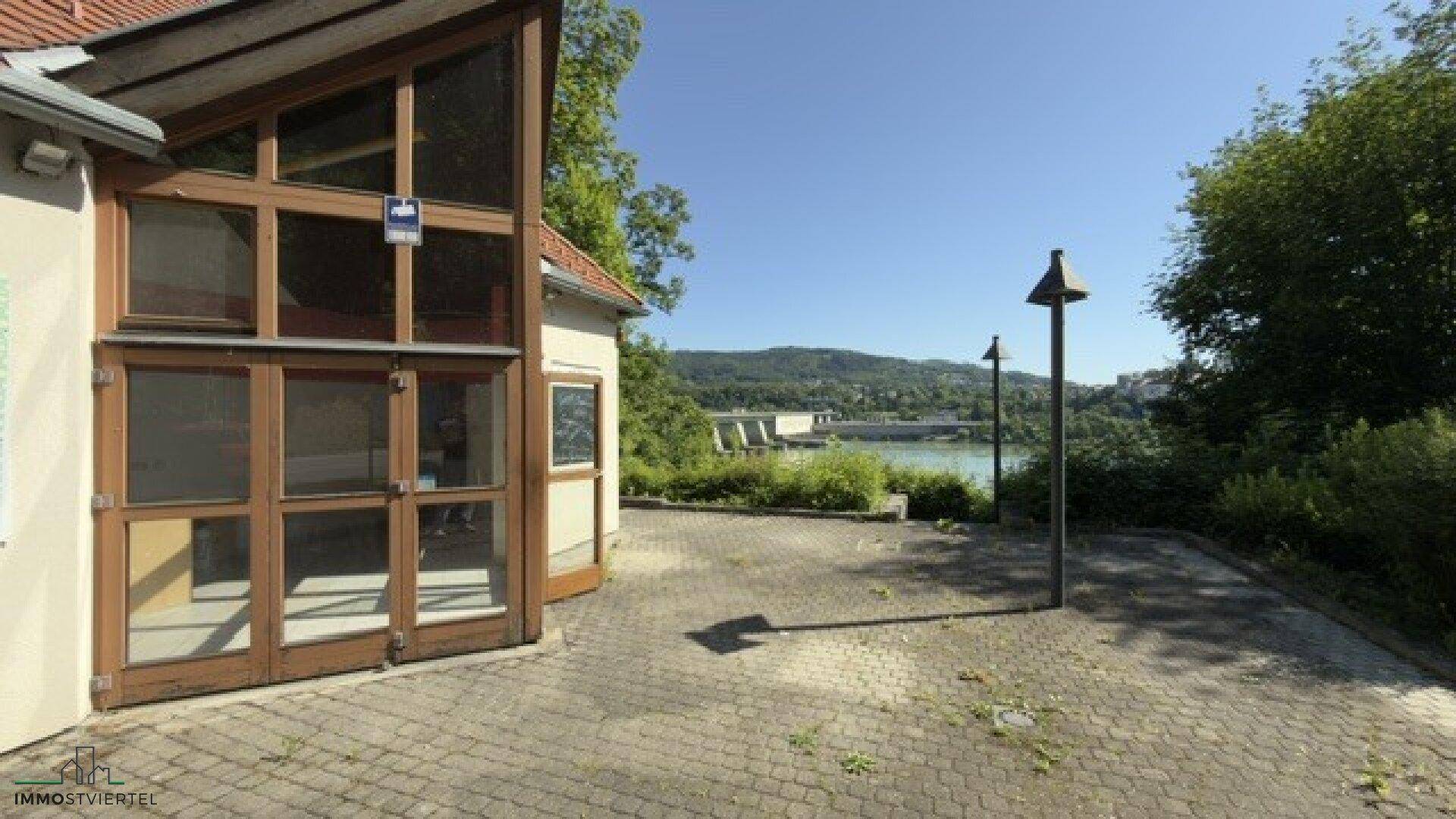 Gepflasterter Außenbereich neben dem Gebäude mit Blick auf den Fluss und die umliegende Natur.