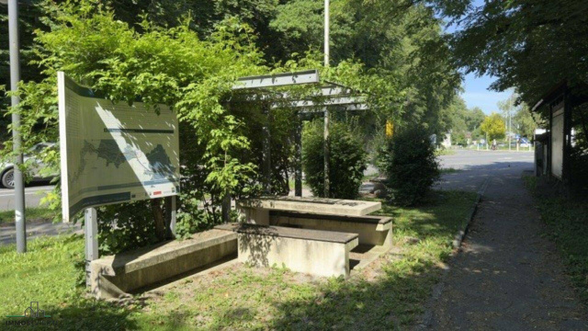 Informationsbereich im Freien mit einer großen Karte und robusten Betonbänken unter einer Pergola.