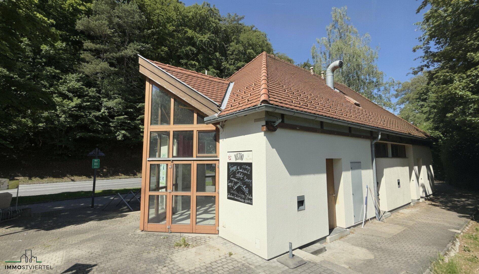Seitenansicht des Gebäudes mit markantem Dachüberstand, Glasfront und einem Schornstein auf dem Dach.
