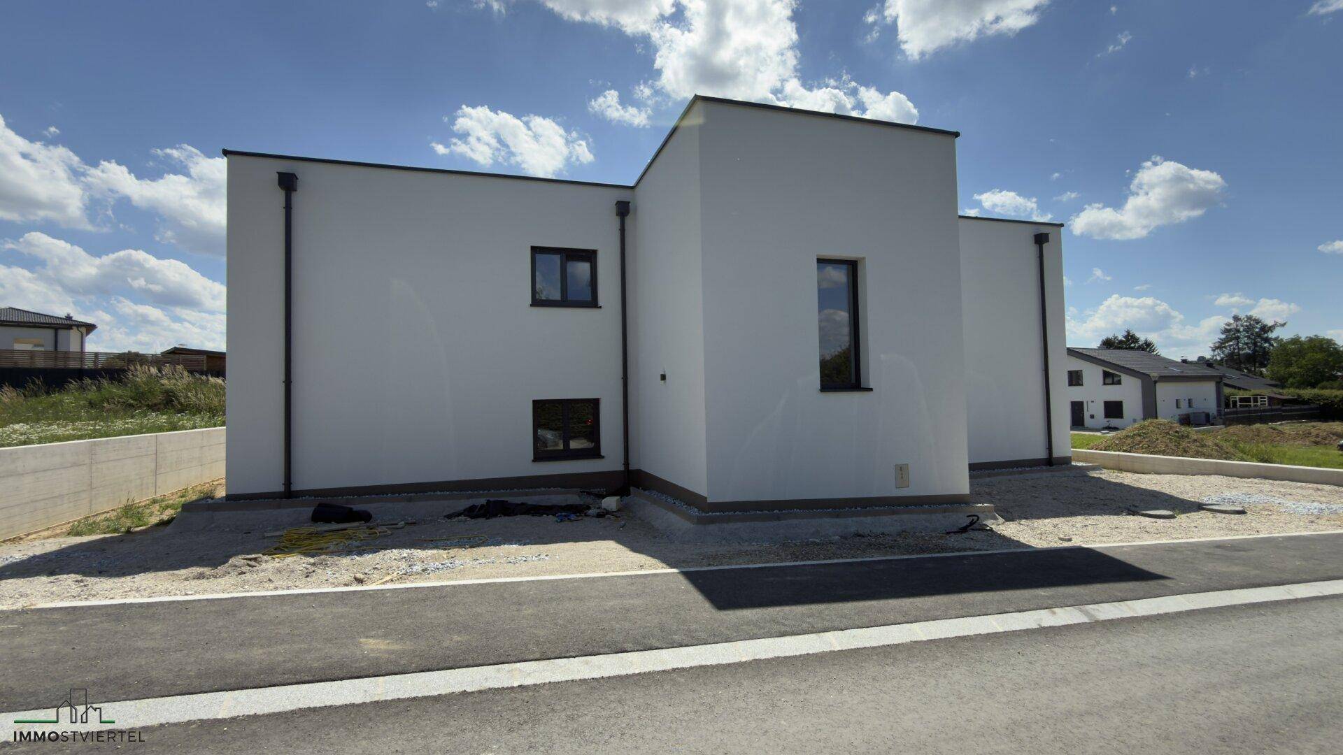 Moderne weiße Fassade eines Neubaus mit klaren Linien und minimalistischem Design unter blauem Himmel.
