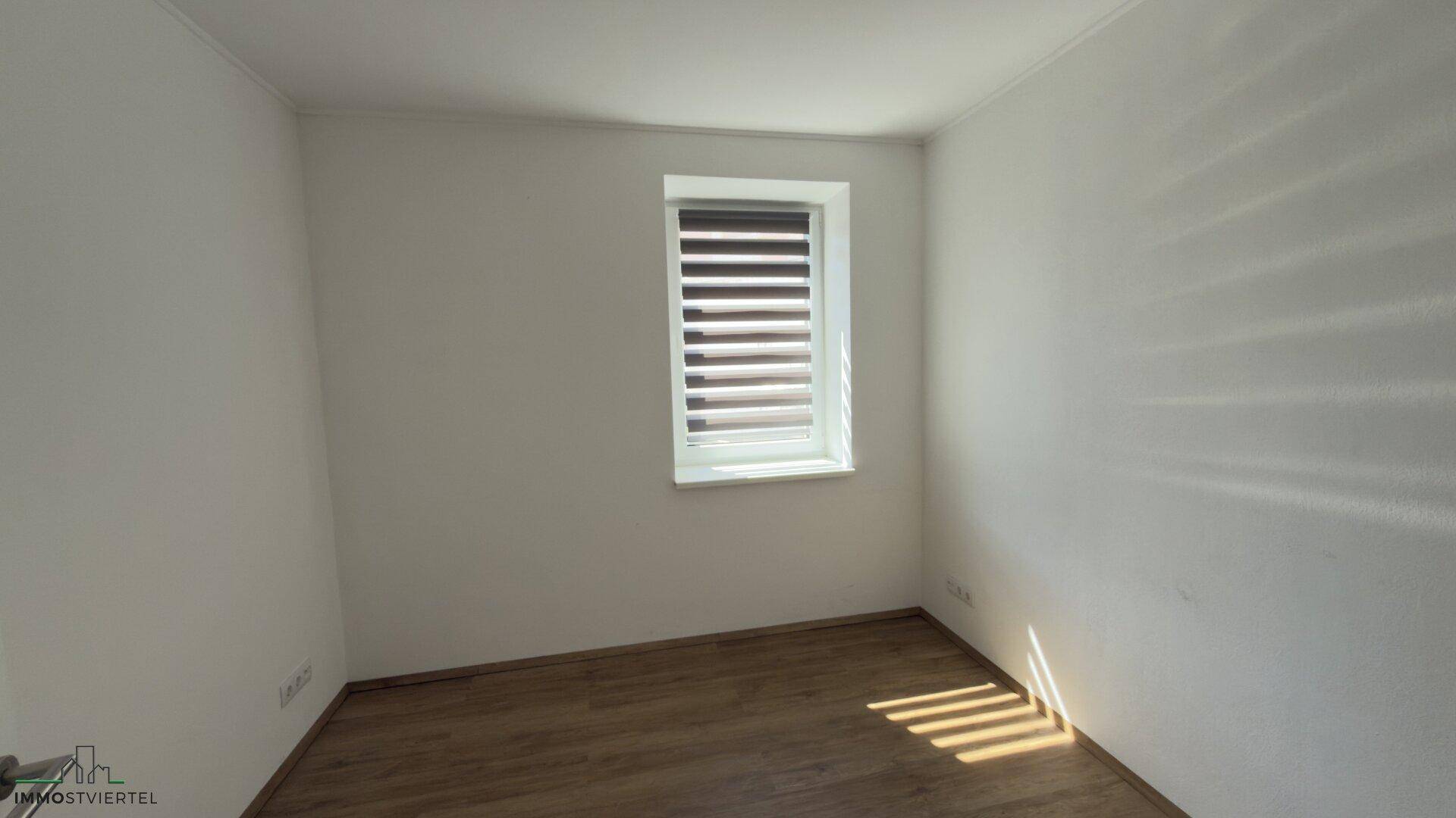 Helles Schlafzimmer mit Holzboden und einem Fenster, das natürliches Licht hereinlässt.