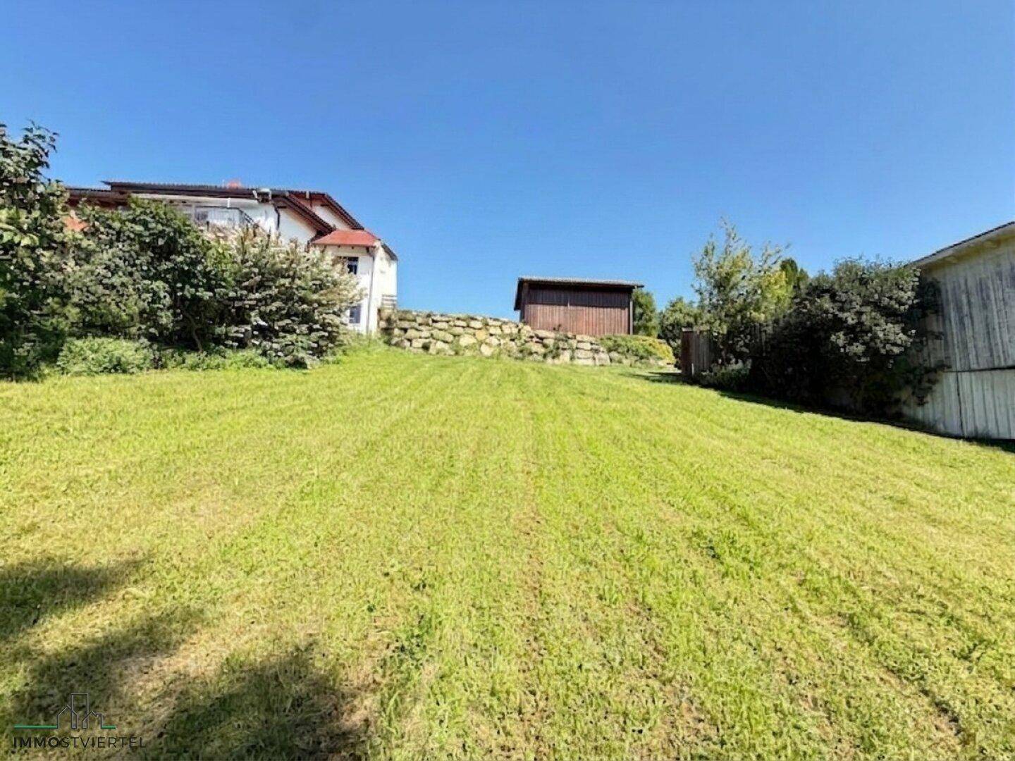 Große, gepflegte Rasenfläche mit einem Gartenhaus im Hintergrund und einem Steinwall.