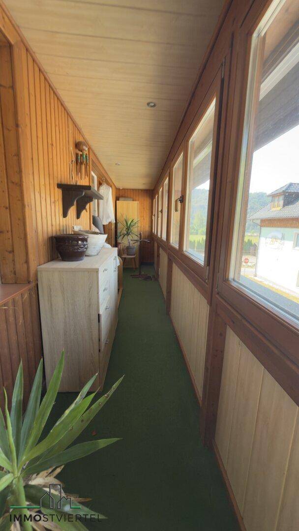 Verglaster Balkon oder Wintergarten mit Holzverkleidung und langen Fensterfronten.