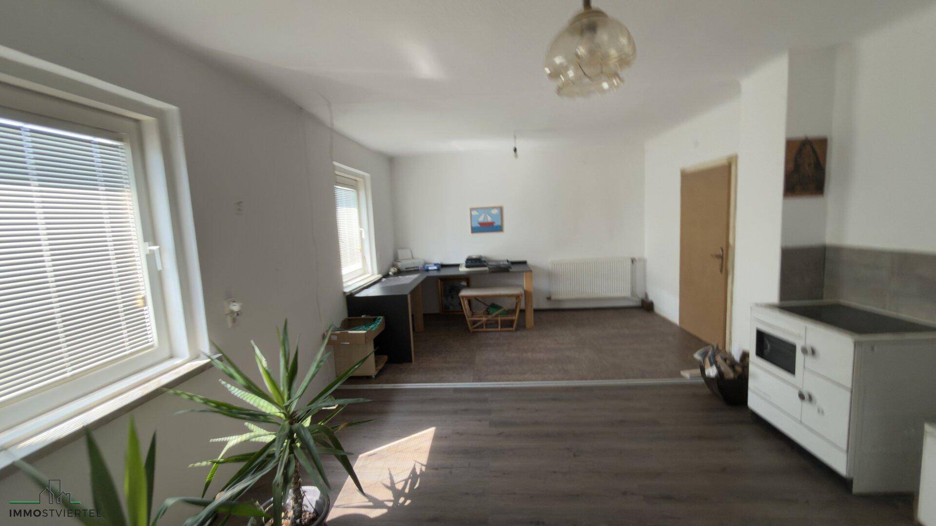 Helles Zimmer mit Schreibtisch, Fenstern und einem traditionellen Ofen.
