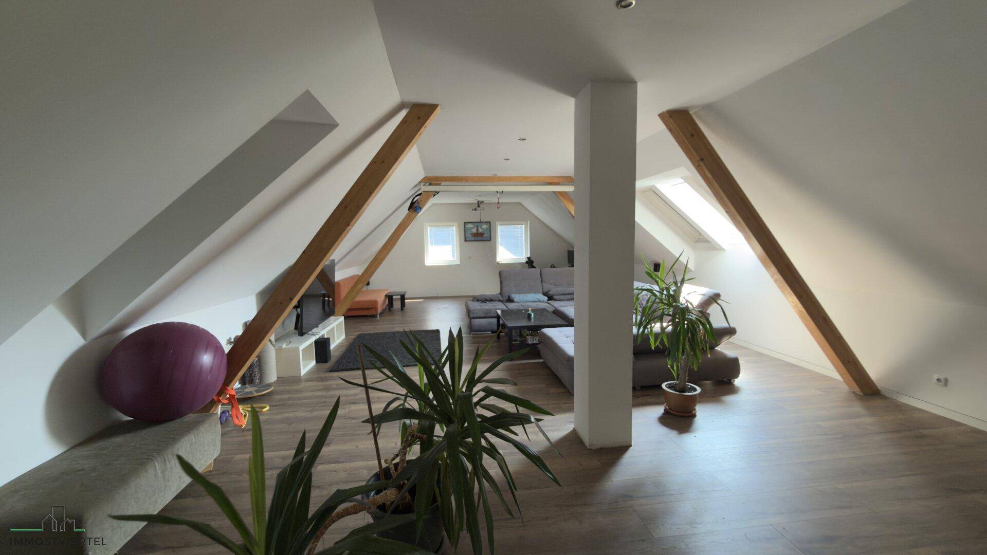 Gemütlicher Wohnbereich im Dachgeschoss mit sichtbaren Holzbalken und Dachfenstern.