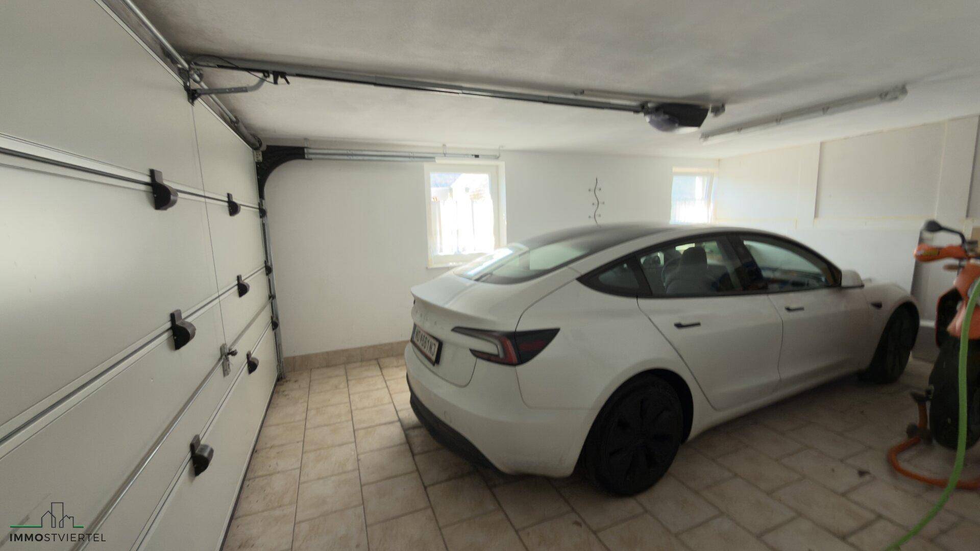 Geräumige Garage mit einem Elektrofahrzeug und Fliesenboden.