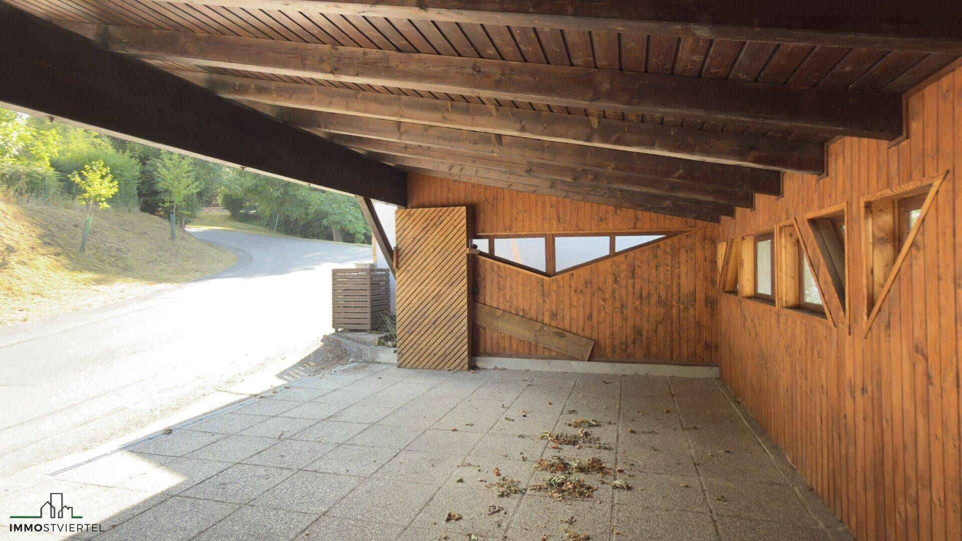 Überdachter Stellplatz oder Carport mit Holzverkleidung und Blick auf die Zufahrtsstraße.