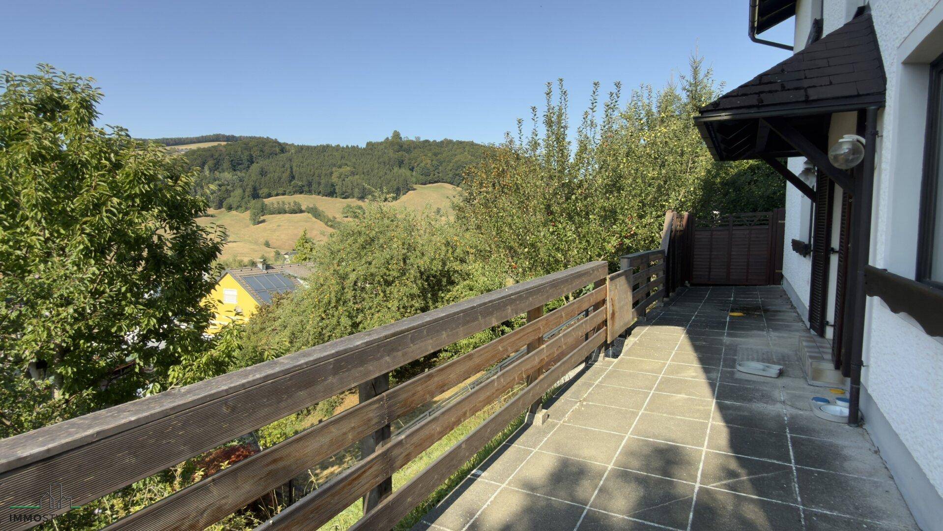 Langer Balkon mit Fliesenboden und Holzgeländer, bietet weiten Blick auf die grüne Hügellandschaft.