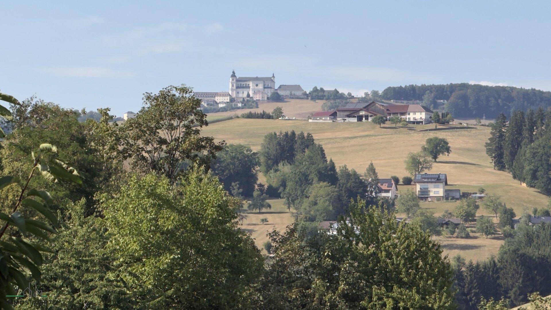 Malerischer Fernblick über sanfte Hügel und ländliche Bebauung unter blauem Himmel.