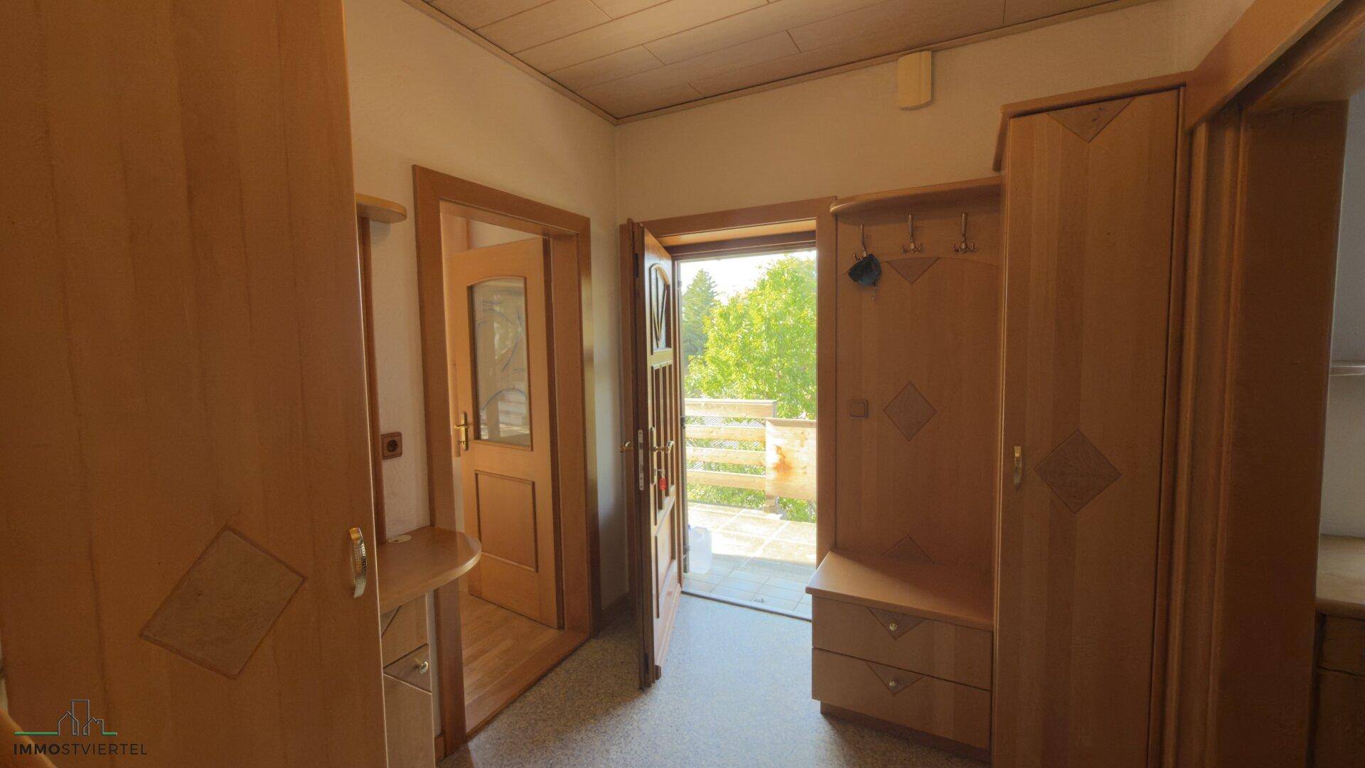 Heller Eingangsbereich mit Garderobe aus Holz und Zugang zu einem Außenbereich.