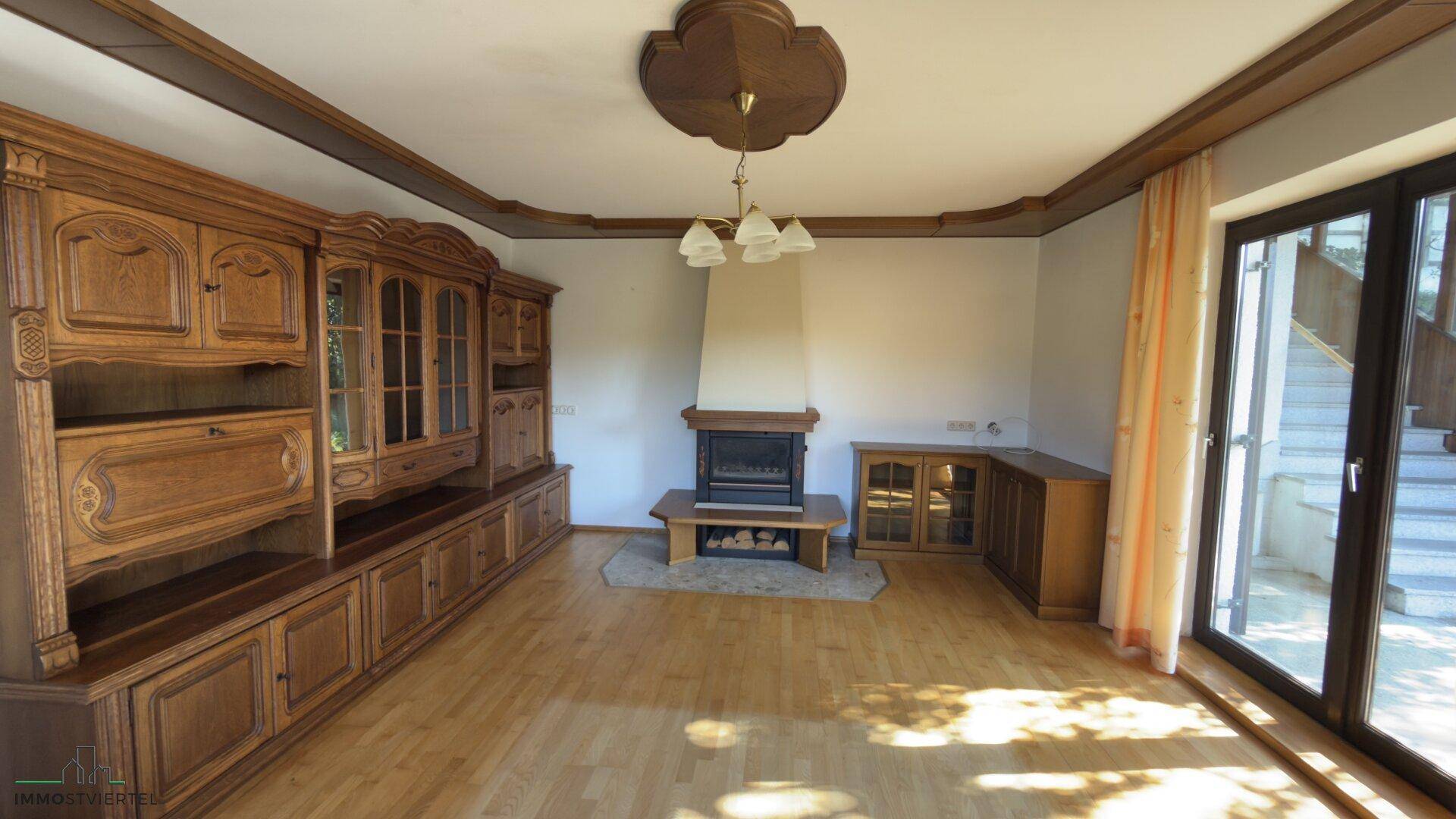 Geräumiges Wohnzimmer mit Holzboden, Kamin und großen Fenstern zum Garten.
