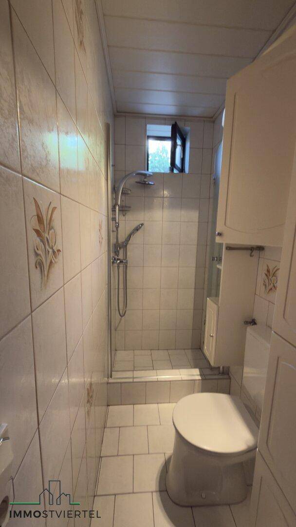 Kleines Badezimmer mit Dusche, WC und hellen Fliesen, inklusive Fenster.