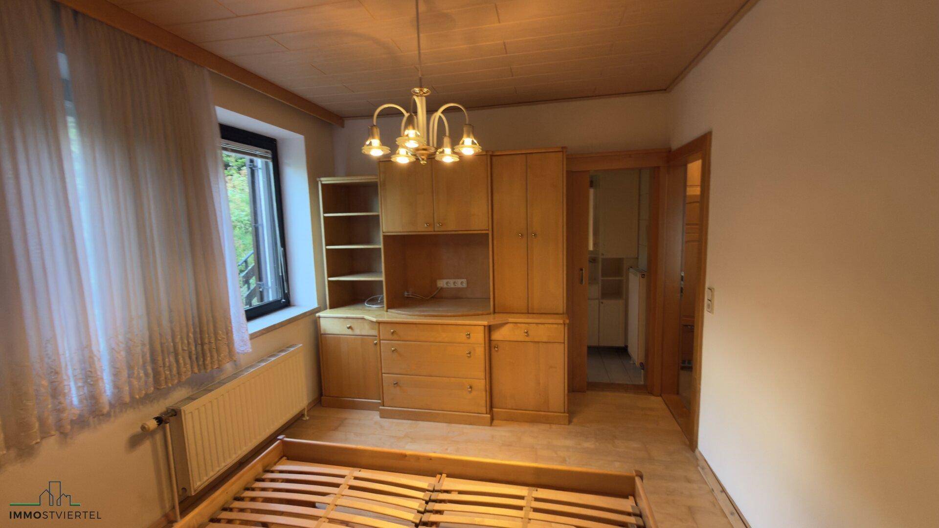 Schlafzimmer mit Holzboden, großem Fenster und Einbauschrank aus hellem Holz.
