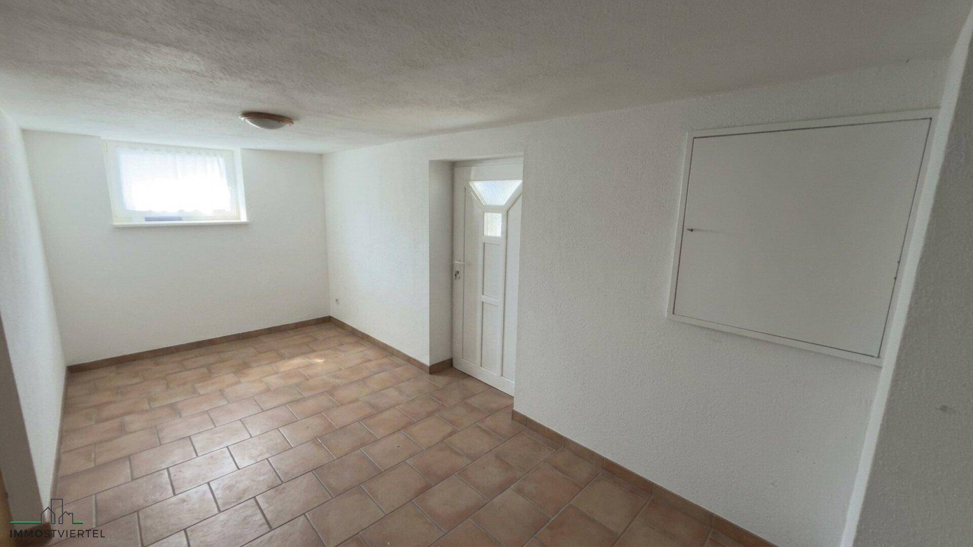 Leerer Raum im Untergeschoss mit Fliesenboden und einem kleinen Fenster.