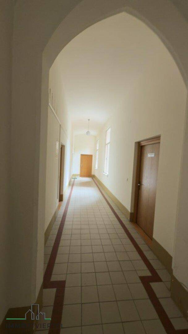 Langer Flur mit Fliesenboden, hohen Decken und natürlichem Lichteinfall durch Fenster.
