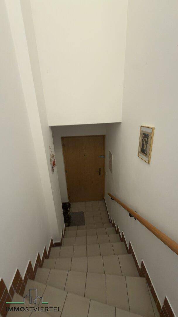 Schlichtes Treppenhaus mit Fliesenstufen und Holzhandlauf, das in den unteren Bereich führt.