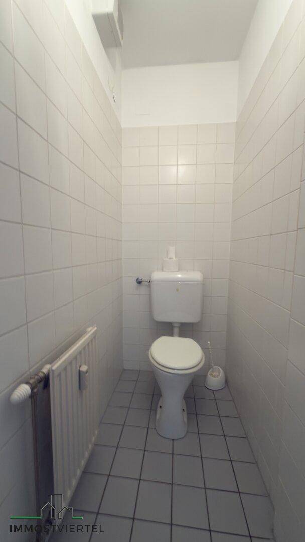 Kleines Gäste-WC mit weißer Toilette und hellen Fliesen an Wänden und Boden.