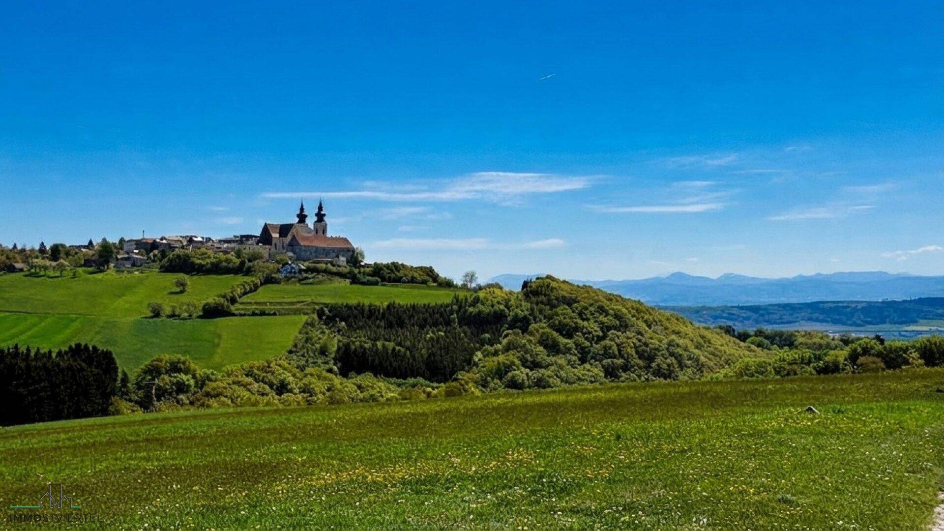 Weitläufige grüne Hügellandschaft mit einem Dorf und einer Kirche auf einem Hügel im Hintergrund.