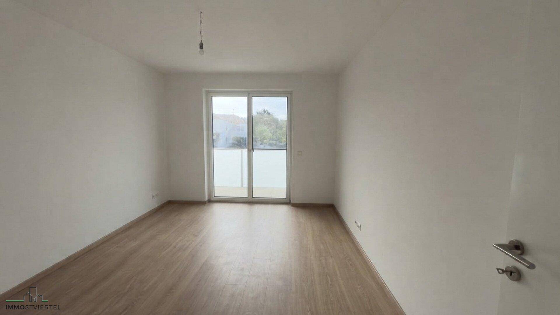 Helles Schlafzimmer mit Laminatboden und direktem Zugang zu einem Balkon.
