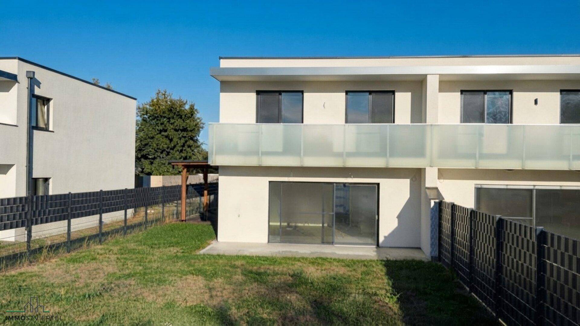 Rückseite des modernen Doppelhauses mit privatem Garten und Terrasse unter blauem Himmel.