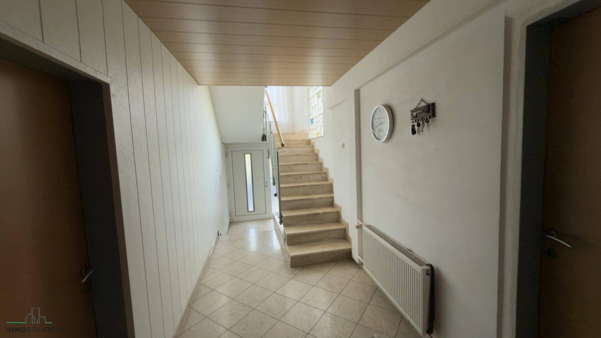 Heller Flur mit Treppenaufgang, Holzdeckenverkleidung und Fliesenboden.