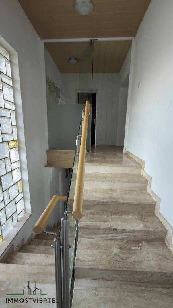 Marmortreppe mit modernem Geländer und farbigem Glasfenster für natürliches Licht.