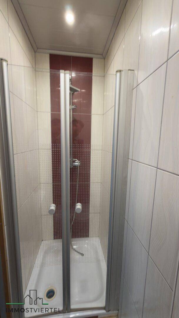 Duschkabine mit Fliesenwänden und einfacher Duscharmatur, funktional und hell.