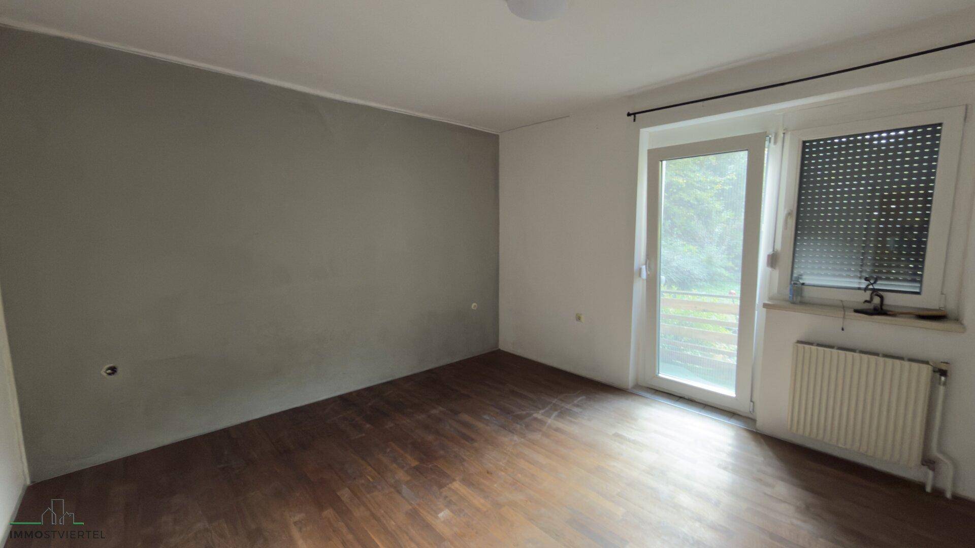 Schlafzimmer mit Holzboden, grauer Akzentwand und Zugang zum Balkon.