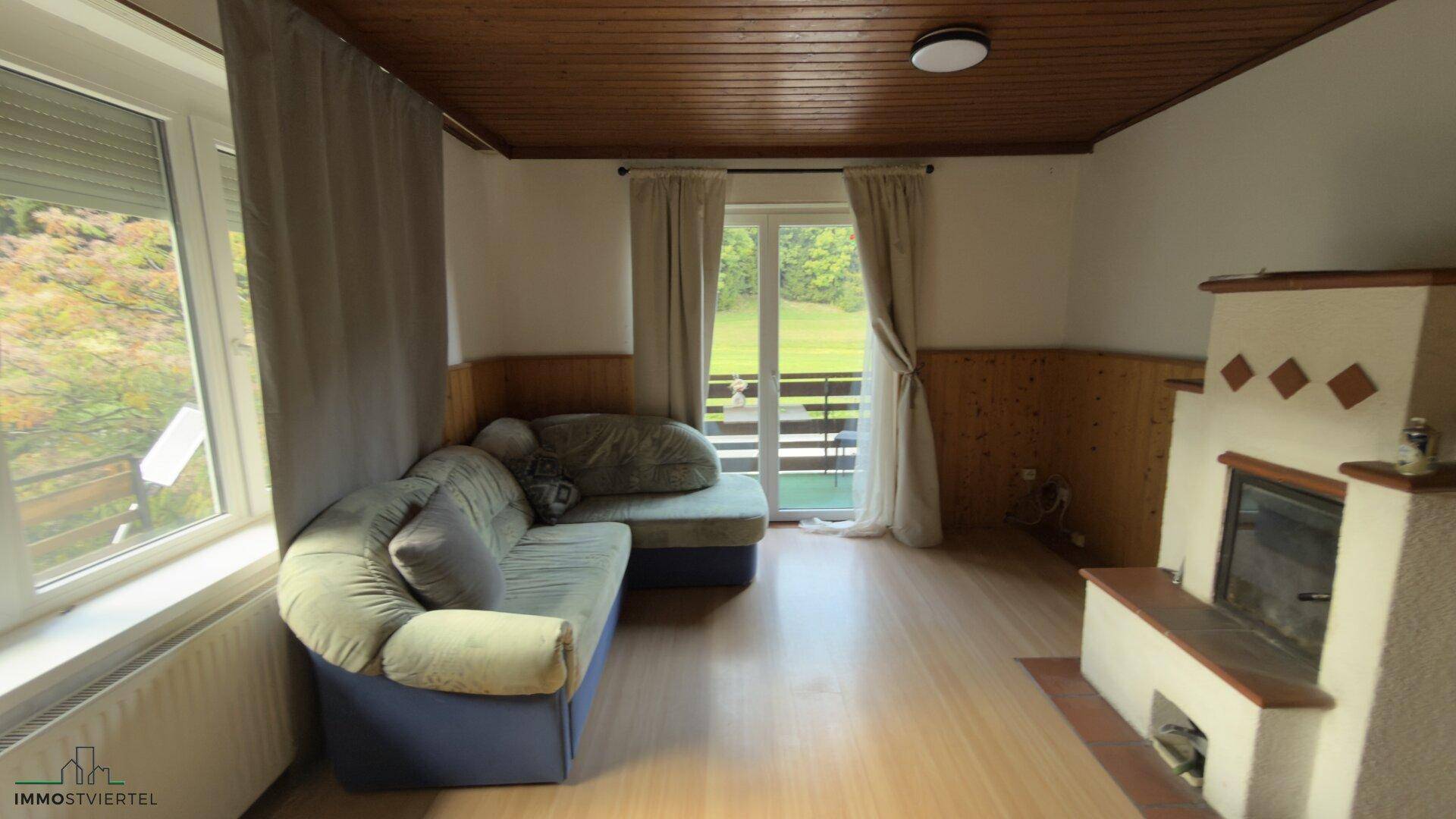 Gemütliches Wohnzimmer mit Kamin, Holzdecke und Zugang zum Balkon.