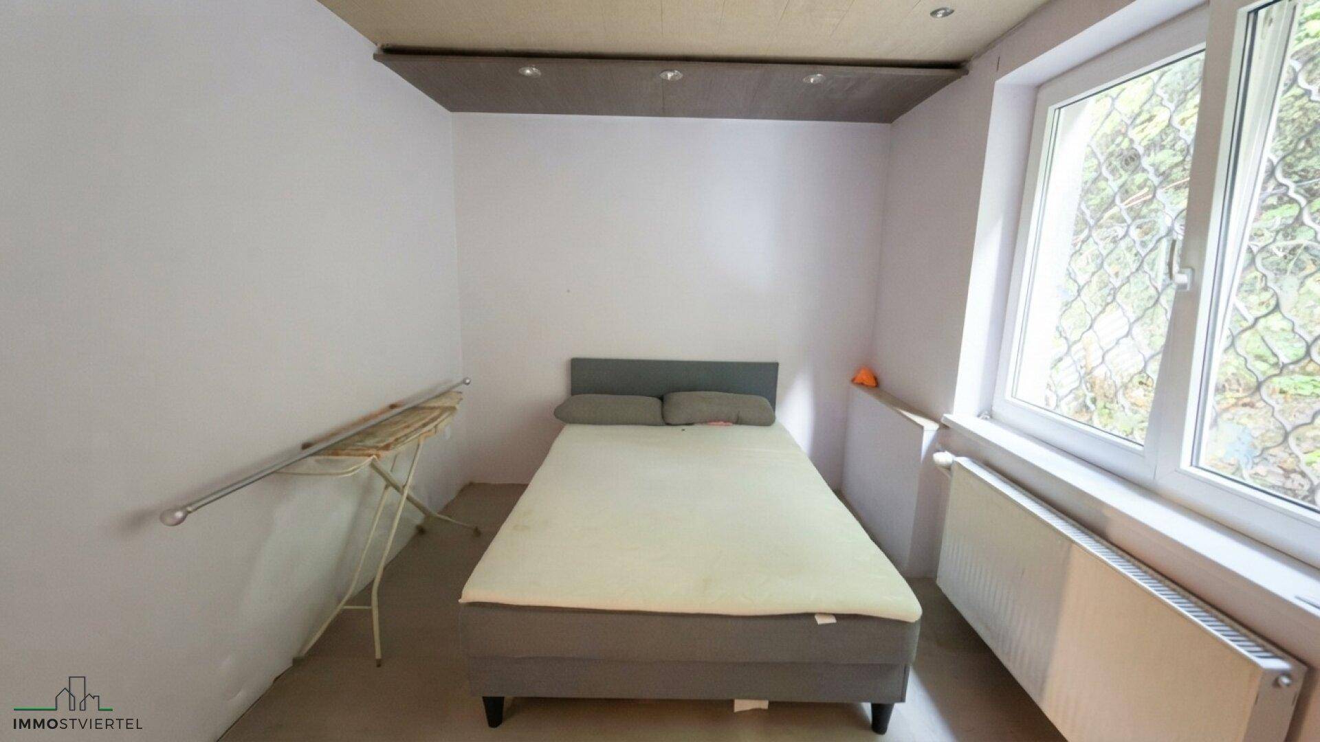 Schlichtes Schlafzimmer mit Doppelbett, Fenster und Heizkörper, hell und funktional.