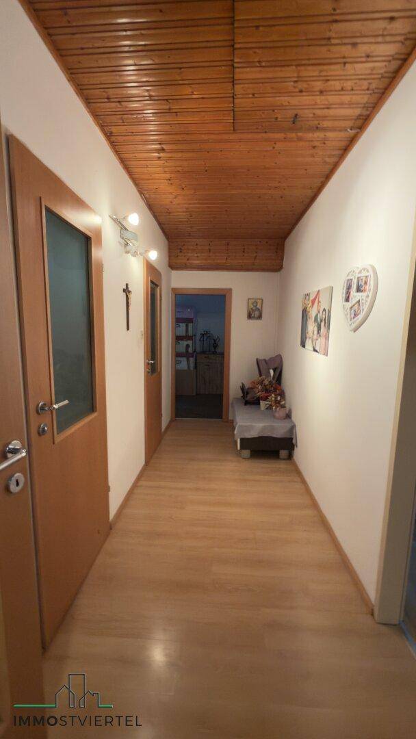 Langer Flur mit Holzdeckenverkleidung und hellem Laminatboden, gut beleuchtet.
