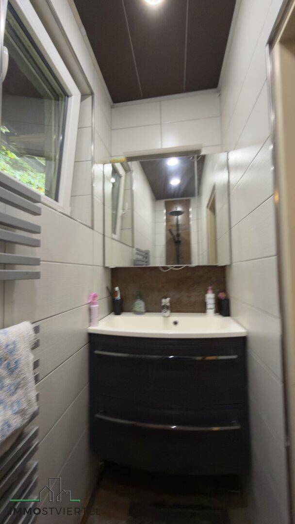 Badezimmer mit Waschtisch, Spiegelschrank und Fenster für Tageslicht.