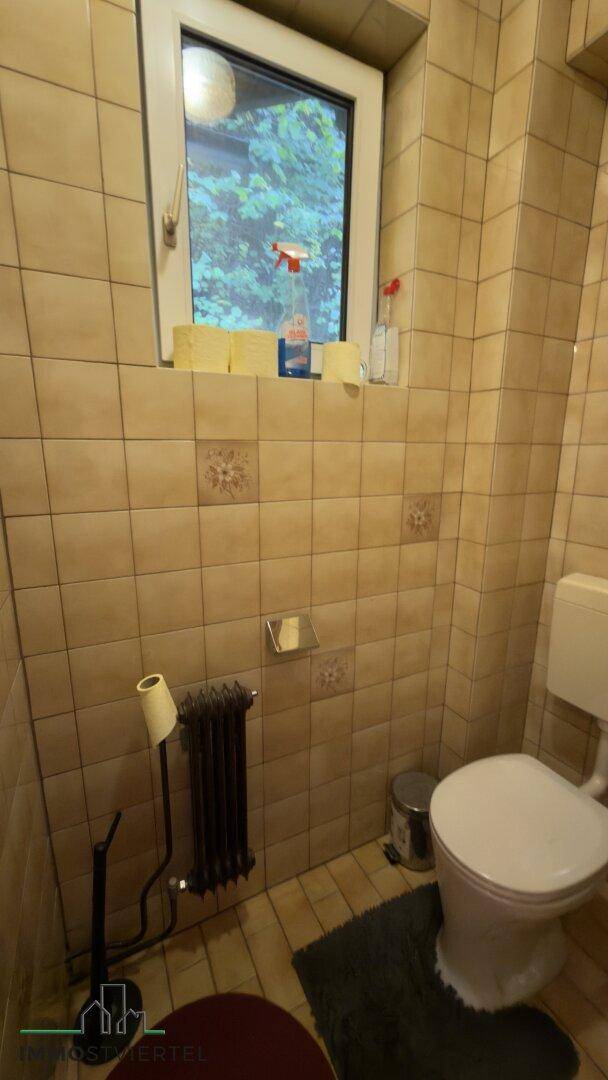 Gäste-WC mit Fenster, Fliesenboden und Heizkörper, praktisch und hell.