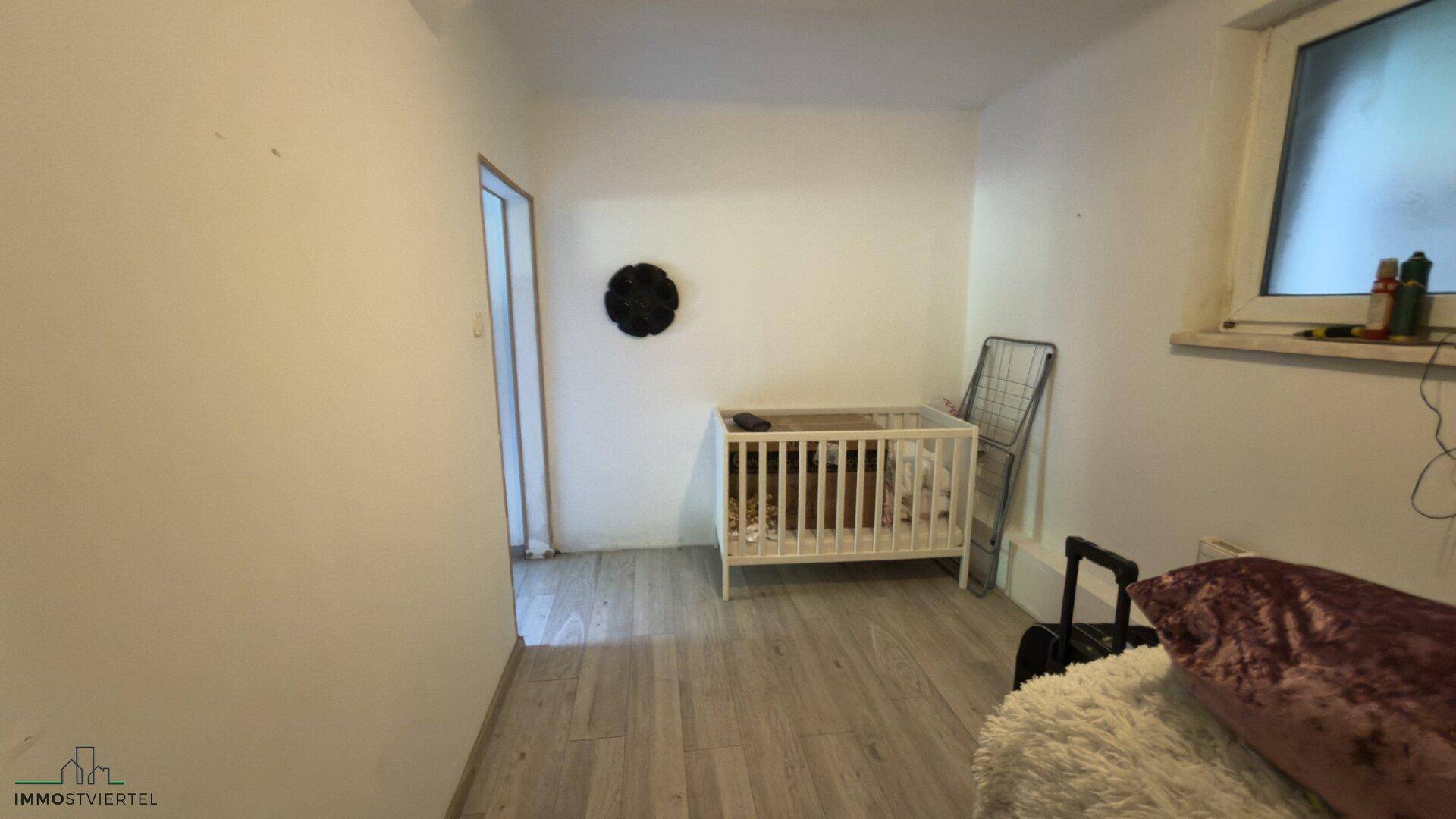 Kleines Zimmer mit Babybett und hellem Bodenbelag, ideal als Kinderzimmer.