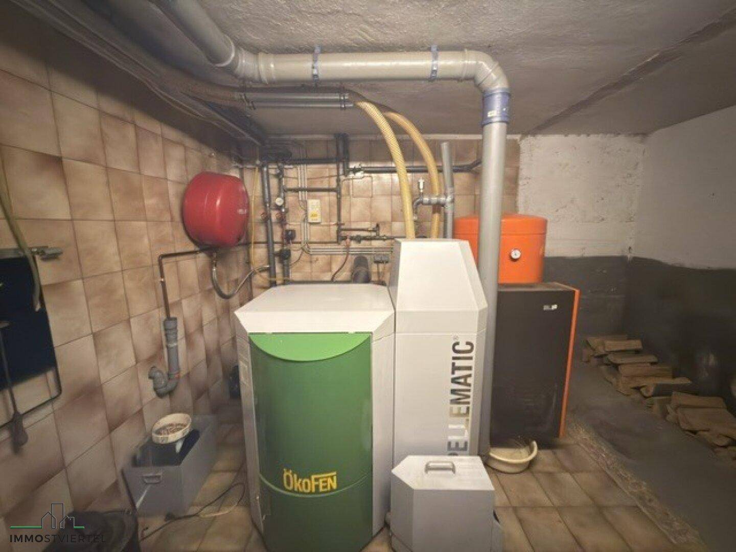 Heizraum mit moderner Pelletheizung und Warmwasserspeicher in gefliestem Kellerbereich.