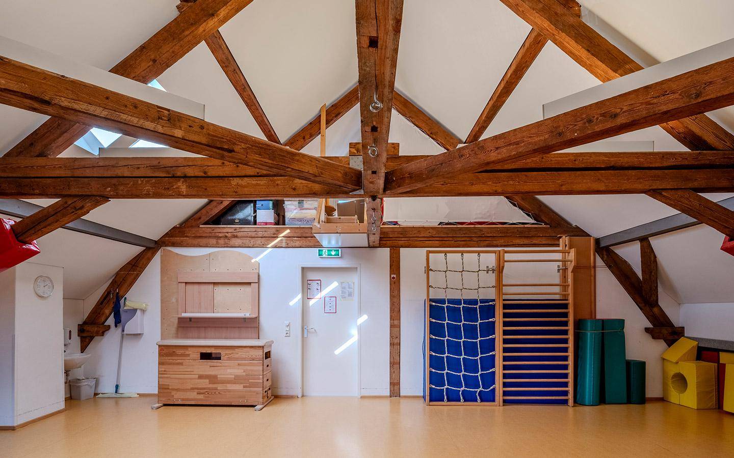 Großer Raum mit sichtbaren Holzbalken und Sportgeräten, ideal für Bewegung und Spiel.