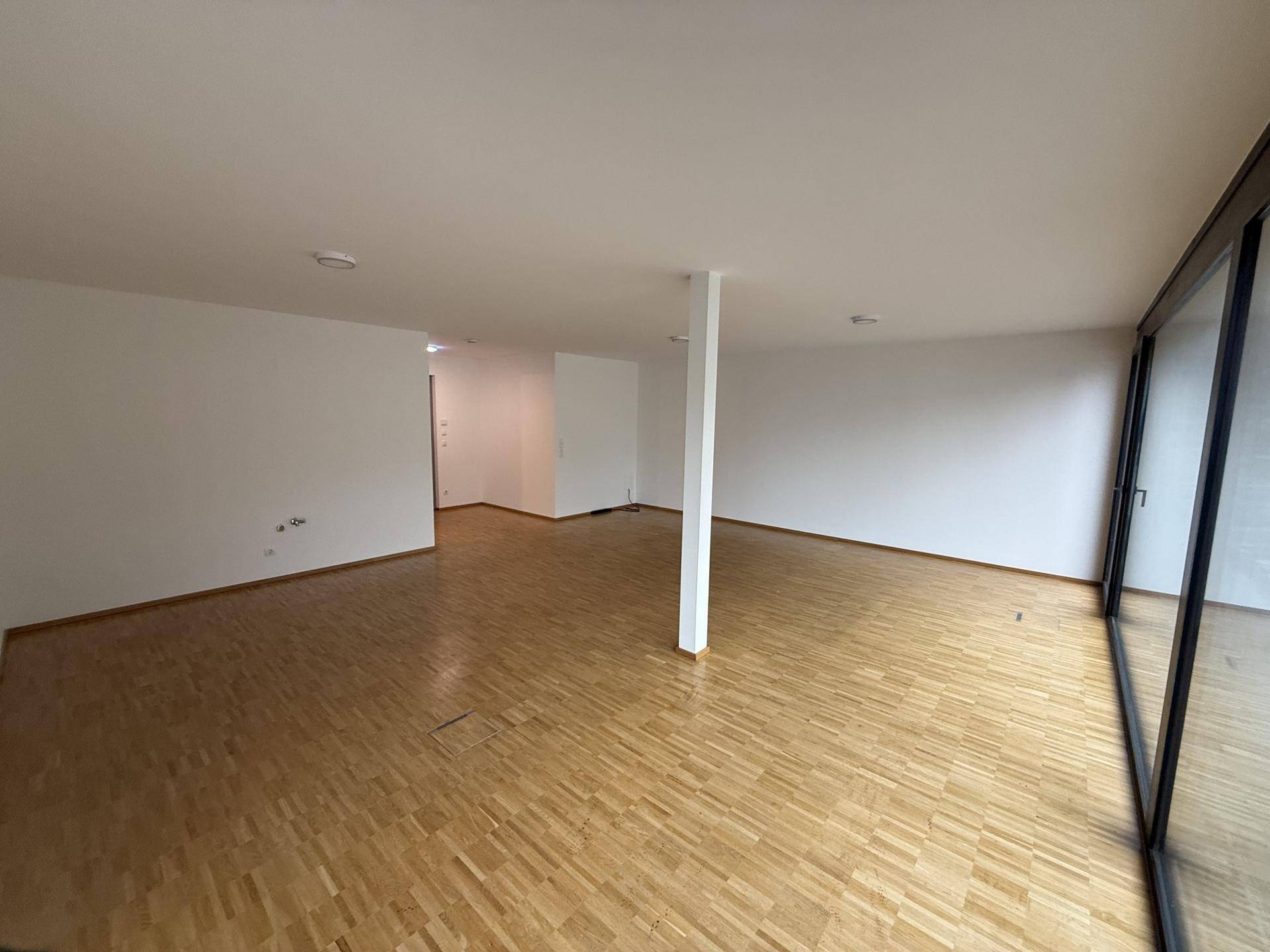 Heller, leerer Raum mit Holzboden und großen Fenstern, die viel Tageslicht hereinlassen und eine offene Atmosphäre schaffen.