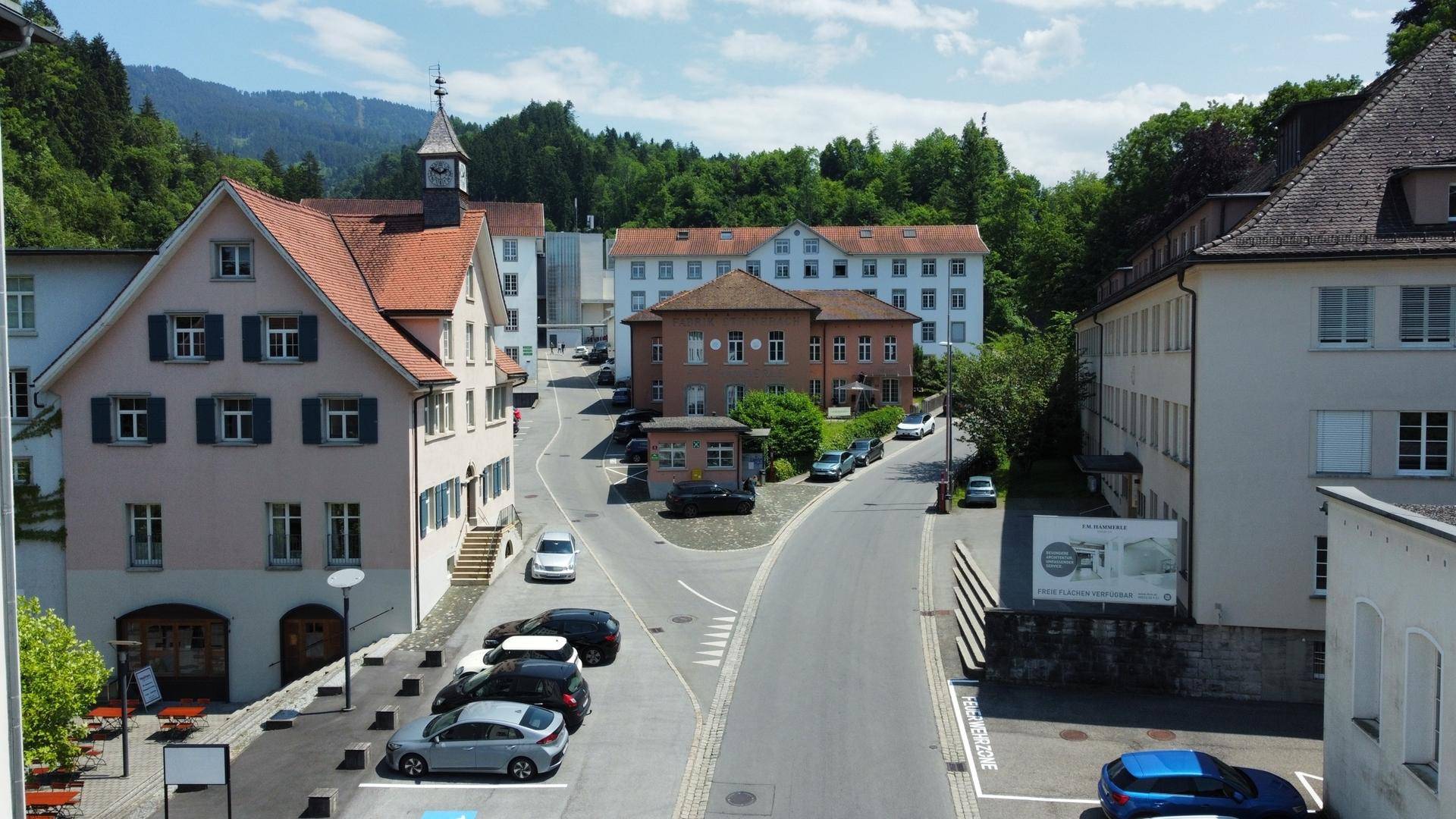 Panoramablick auf eine ländliche Straße mit historischen Gebäuden und bewaldeten Hügeln im Hintergrund.