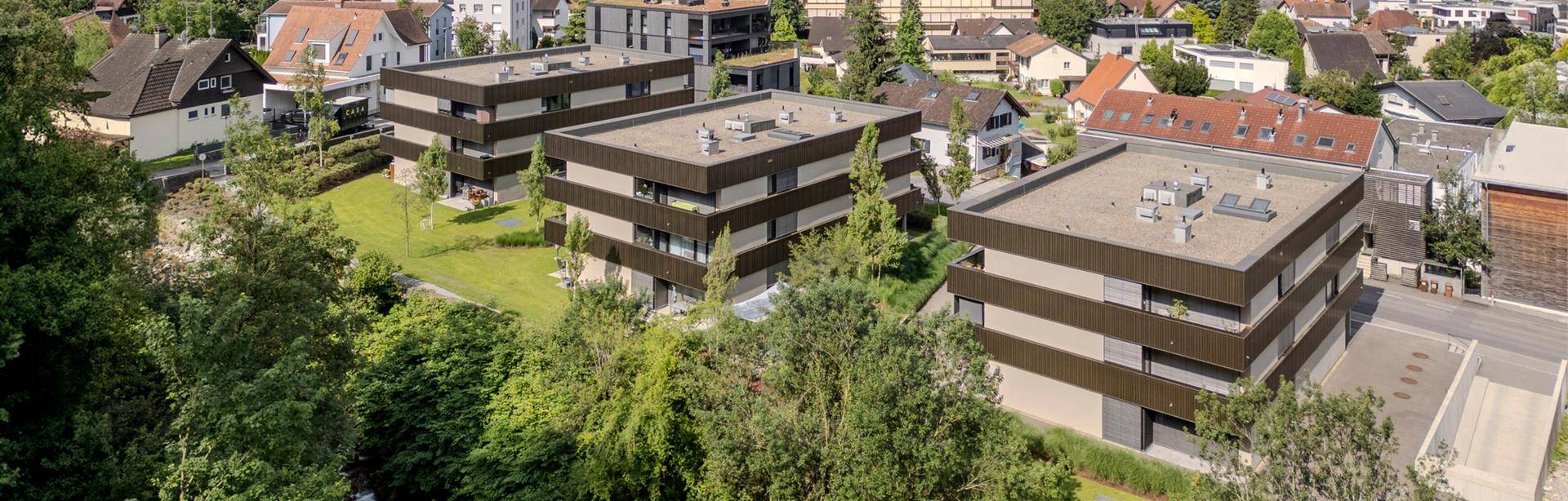 Luftaufnahme einer modernen Wohnanlage mit mehreren Gebäuden, umgeben von Bäumen und einer dichten Wohnbebauung.