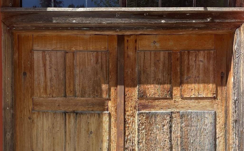 Nahaufnahme einer rustikalen, abgenutzten Holztür mit sichtbarer Maserung und Patina, die den Charme des Gebäudes unterstreicht.